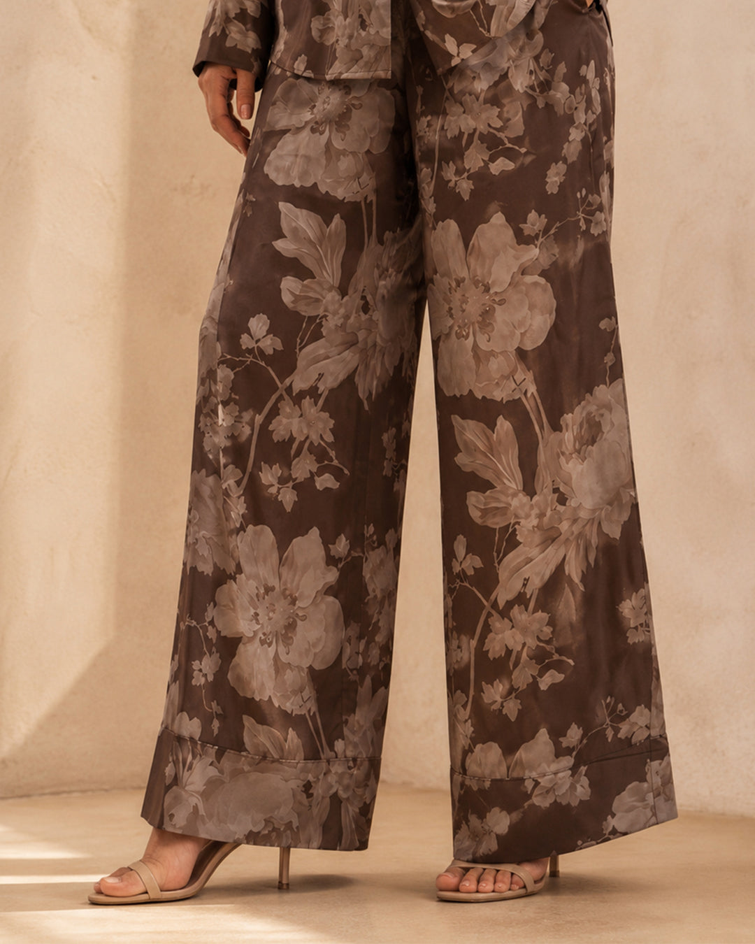 Close-up of Sahara Bloom bronze wide-leg silk trousers showing the contrasting light floral pattern.