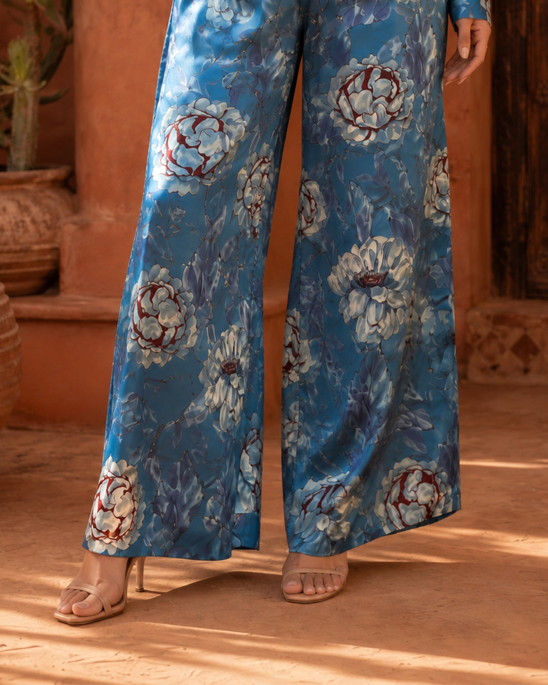 Close-up of Sahara Bloom blue wide-leg silk trousers with large pale floral motifs and flowing hems.