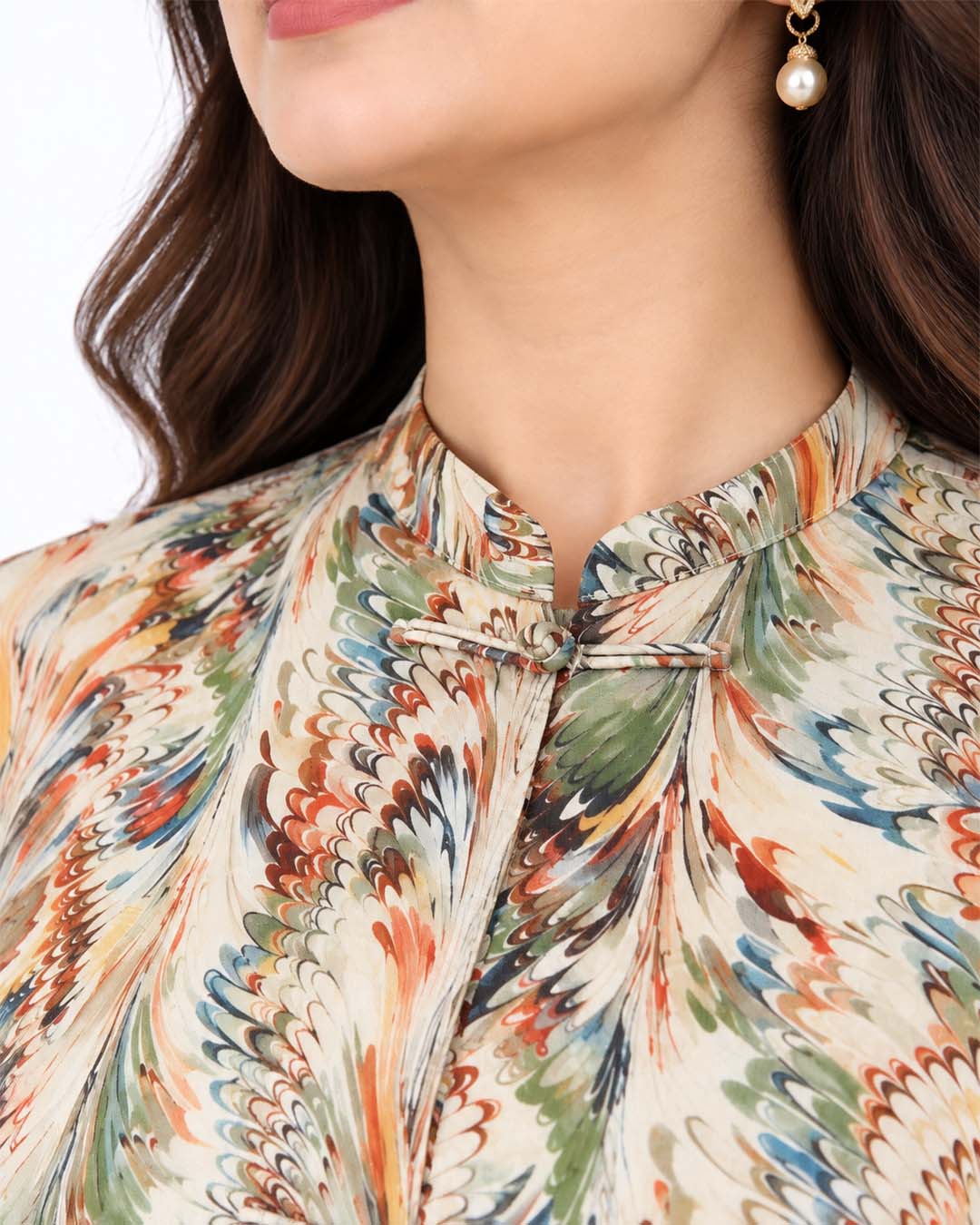 Close-up of the L’Artiste shirt’s stand collar, decorative loop fastening and multicolour print on a beige base.